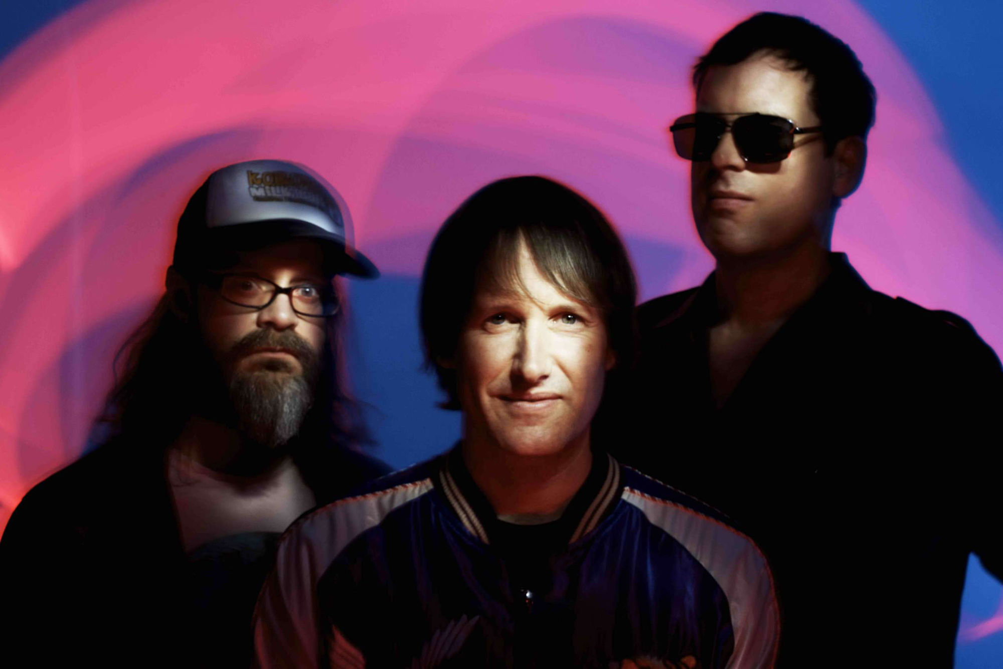 Promo photo of the band Ash facing the camera against a blue and pink marble swirl background.